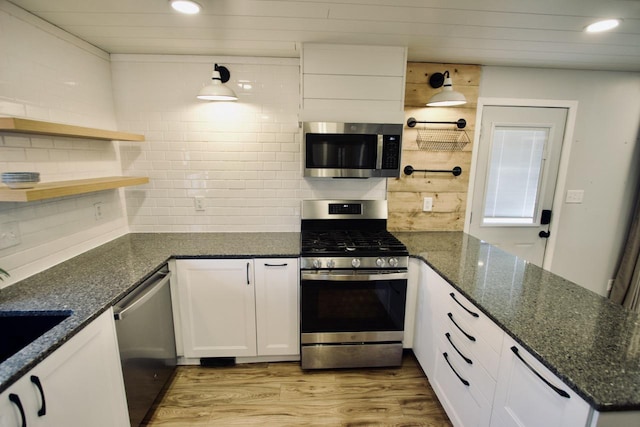 kitchen featuring white cabinets, appliances with stainless steel finishes, tasteful backsplash, light hardwood / wood-style floors, and dark stone countertops