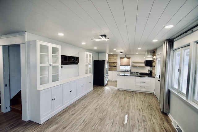 kitchen with white cabinets, light wood-type flooring, and stainless steel fridge