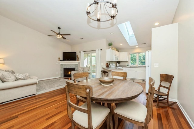 dining area featuring vaulted ceiling with skylight, ceiling fan with notable chandelier, and hardwood / wood-style flooring