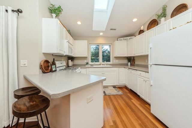 kitchen featuring white appliances, white cabinets, a skylight, a kitchen breakfast bar, and kitchen peninsula