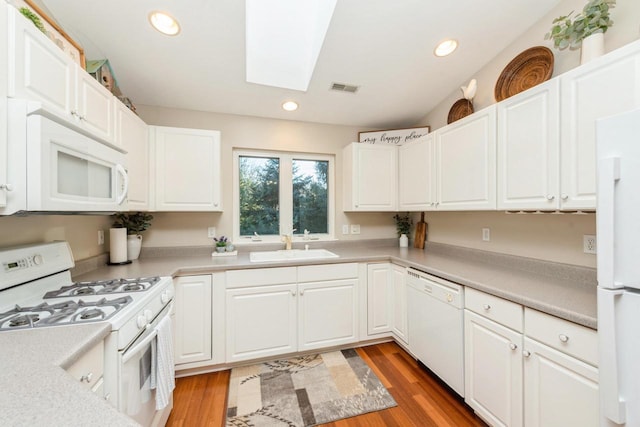 kitchen featuring a skylight, hardwood / wood-style flooring, white appliances, white cabinets, and sink