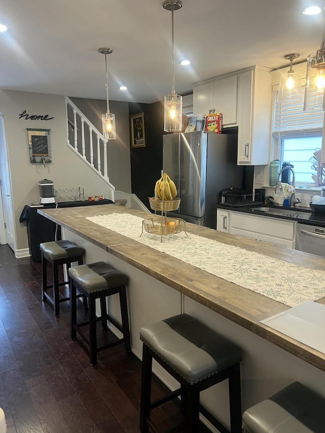 kitchen with pendant lighting, dark wood-type flooring, a breakfast bar, appliances with stainless steel finishes, and white cabinets