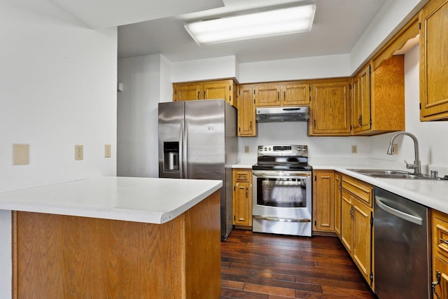 kitchen with dark wood-type flooring, under cabinet range hood, light countertops, appliances with stainless steel finishes, and a sink