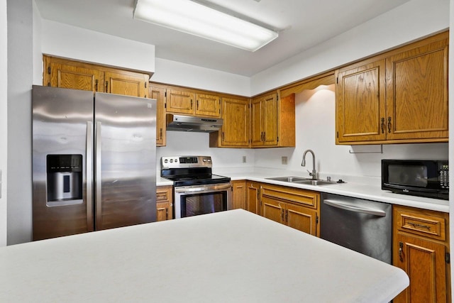 kitchen with under cabinet range hood, light countertops, brown cabinets, appliances with stainless steel finishes, and a sink