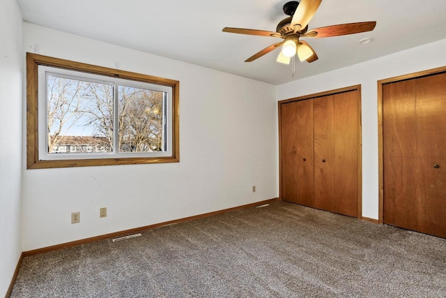 unfurnished bedroom with two closets, baseboards, and carpet floors