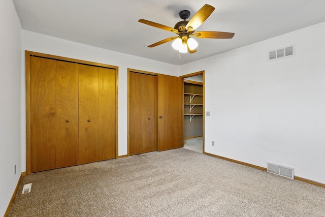 unfurnished bedroom with visible vents, baseboards, two closets, and carpet flooring