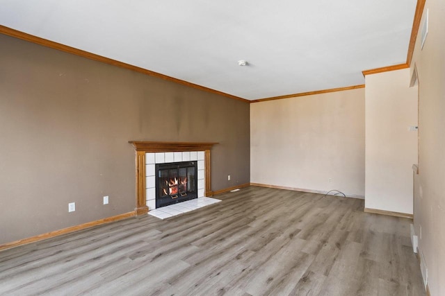 unfurnished living room with a tiled fireplace, crown molding, wood finished floors, and baseboards