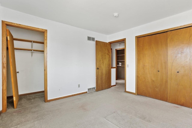 unfurnished bedroom with light carpet, visible vents, baseboards, and multiple closets