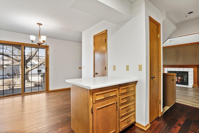 kitchen featuring dark wood-style floors, an inviting chandelier, light countertops, pendant lighting, and a tiled fireplace