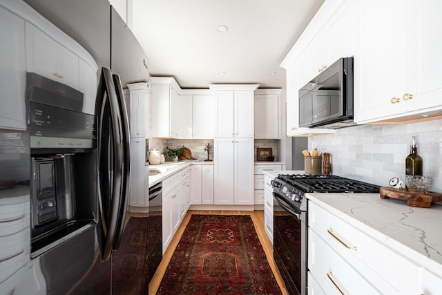 kitchen with white cabinetry, light stone countertops, decorative backsplash, and black appliances