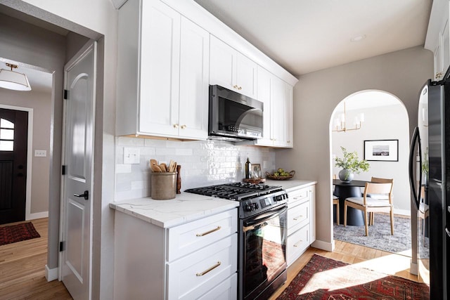 kitchen featuring light hardwood / wood-style flooring, white cabinetry, light stone countertops, black fridge, and range with gas cooktop