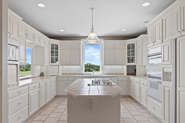 N84W36411 Riverwood Ln, Oconomowoc, WI 53066 - kitchen with light tile patterned floors, tile countertops, decorative backsplash, hanging light fixtures, and a kitchen island