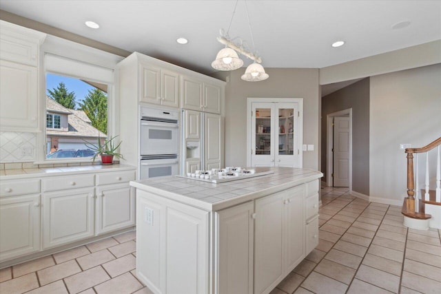 N84W36411 Riverwood Ln, Oconomowoc, WI 53066 - kitchen with tasteful backsplash, tile countertops, a kitchen island, white appliances, and white cabinetry