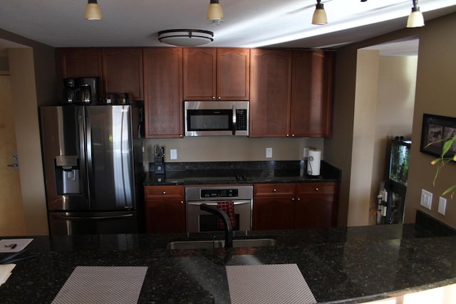 kitchen featuring decorative light fixtures, sink, stainless steel appliances, and dark stone countertops