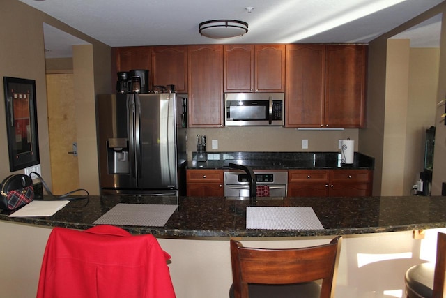 kitchen with kitchen peninsula, appliances with stainless steel finishes, dark stone countertops, and a breakfast bar area