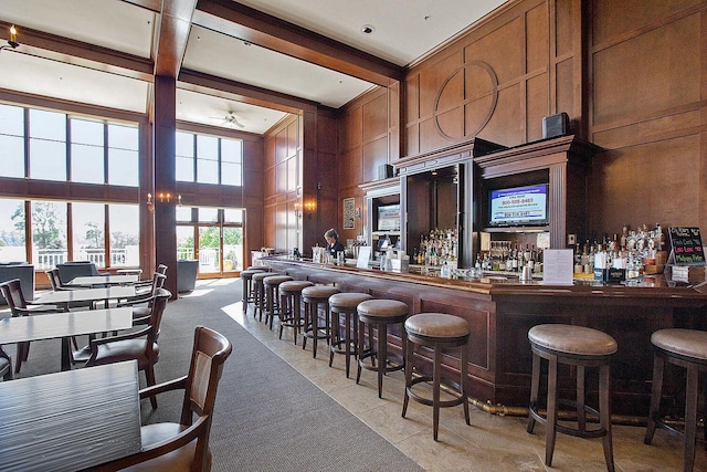 bar featuring beam ceiling, light tile patterned floors, wood walls, and a high ceiling