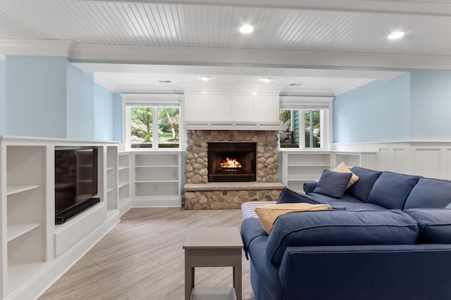 living room featuring light wood-type flooring, built in features, a stone fireplace, and ornamental molding