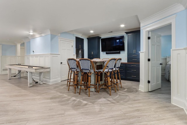 dining space with ornamental molding, light hardwood / wood-style flooring, and bar area