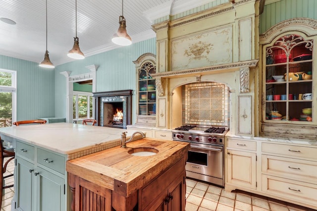 kitchen with decorative light fixtures, sink, a center island with sink, and luxury stove