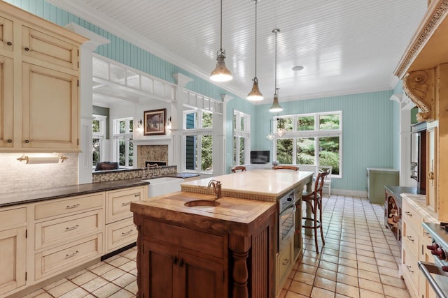 kitchen with pendant lighting, an island with sink, sink, cream cabinets, and crown molding