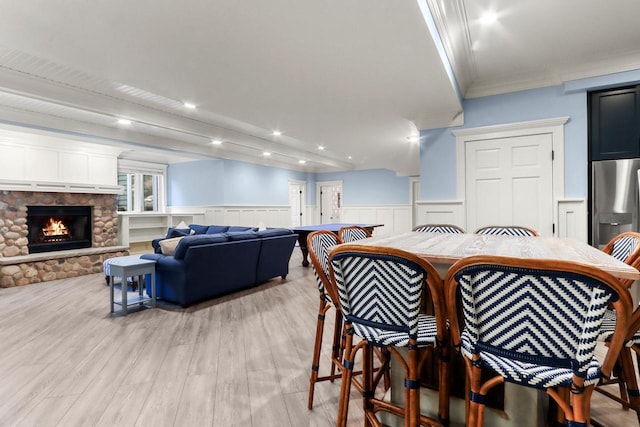 dining room with light wood-type flooring, a stone fireplace, and ornamental molding