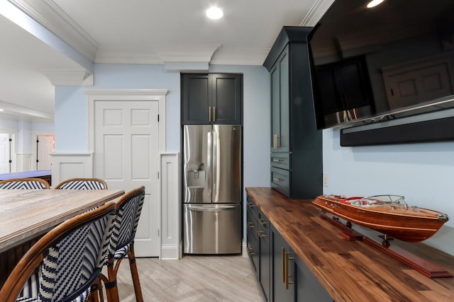 kitchen with light wood-type flooring, ornamental molding, stainless steel fridge, and wooden counters