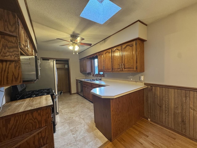 kitchen featuring gas stove, stainless steel dishwasher, kitchen peninsula, wooden walls, and a skylight