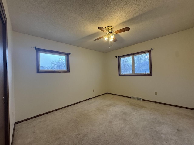 spare room featuring light carpet, ceiling fan, and a textured ceiling