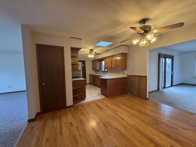 kitchen with ceiling fan, light hardwood / wood-style floors, kitchen peninsula, a skylight, and a textured ceiling