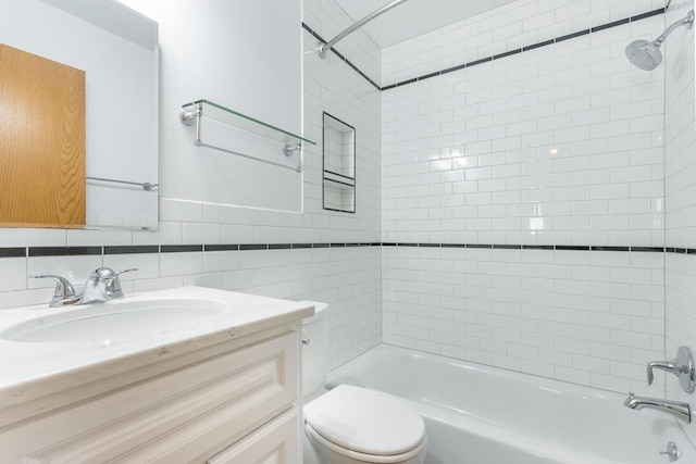 full bathroom featuring tiled shower / bath, vanity, toilet, and tile walls