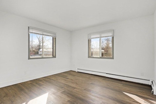 spare room with a healthy amount of sunlight, a baseboard heating unit, and dark hardwood / wood-style floors