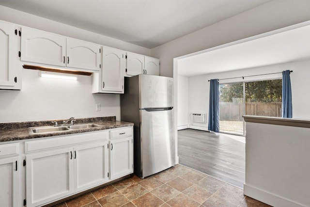 kitchen with a wall unit AC, white cabinetry, stainless steel fridge, and sink