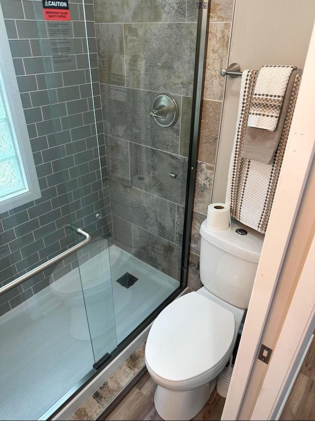 bathroom with a shower with shower door, hardwood / wood-style floors, and toilet