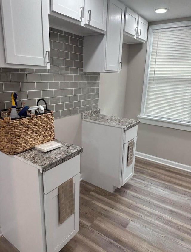 kitchen featuring decorative backsplash, light stone countertops, white cabinets, and light hardwood / wood-style flooring