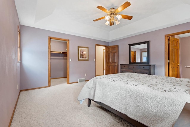 bedroom with a spacious closet, light carpet, a closet, a raised ceiling, and ceiling fan