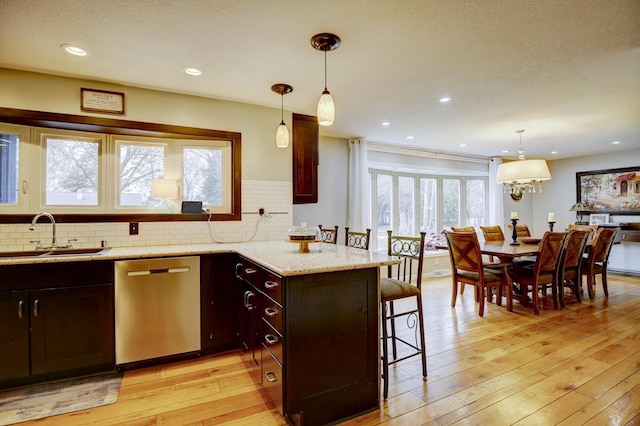 kitchen with dishwasher, hanging light fixtures, light stone countertops, a breakfast bar, and sink