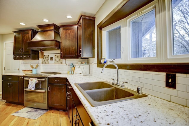 kitchen featuring decorative backsplash, sink, range with two ovens, custom range hood, and light stone counters