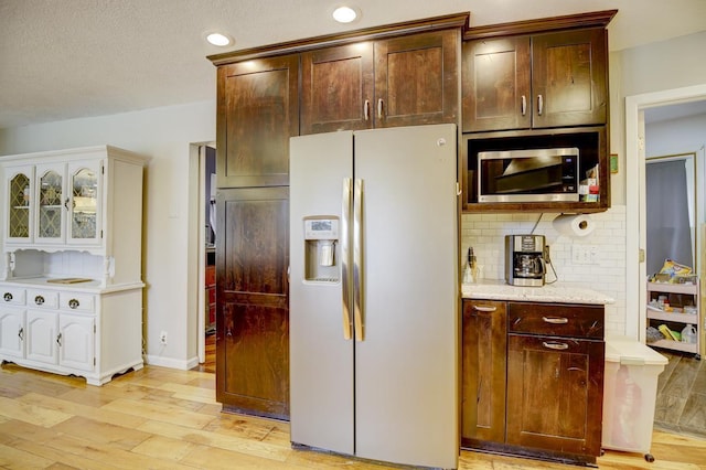 kitchen featuring dark brown cabinetry, stainless steel appliances, backsplash, light wood-type flooring, and light stone counters