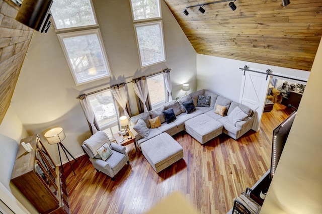 living room with hardwood / wood-style floors, track lighting, a towering ceiling, wood ceiling, and a barn door