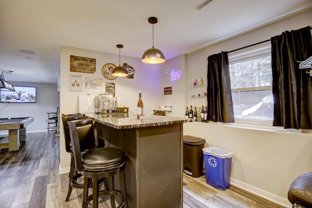 bar with light wood-type flooring, hanging light fixtures, and light stone countertops