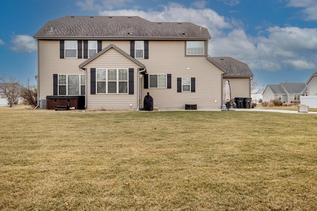 rear view of house with a hot tub and a yard