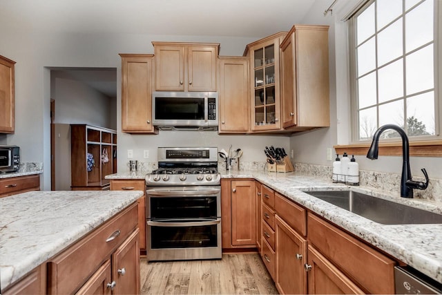 kitchen with light stone countertops, sink, appliances with stainless steel finishes, and light hardwood / wood-style floors