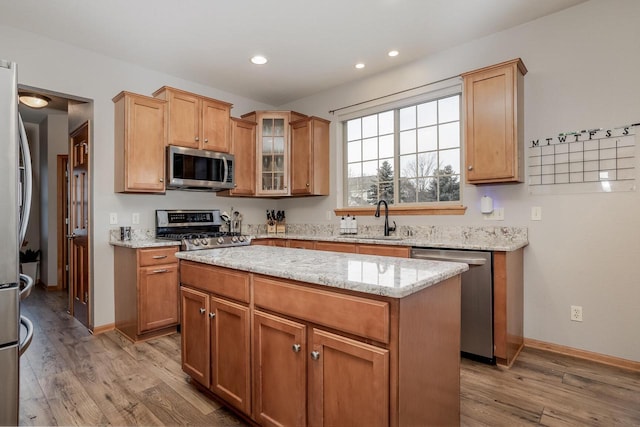 kitchen featuring stainless steel appliances, light wood-type flooring, light stone countertops, a kitchen island, and sink