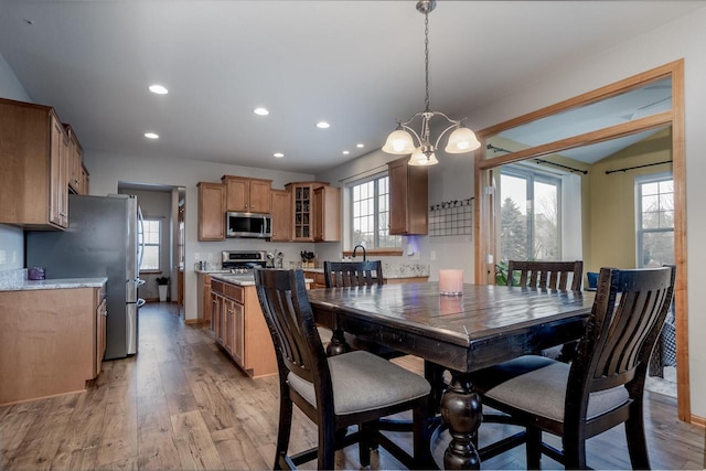 dining space featuring sink, lofted ceiling, an inviting chandelier, and light wood-type flooring