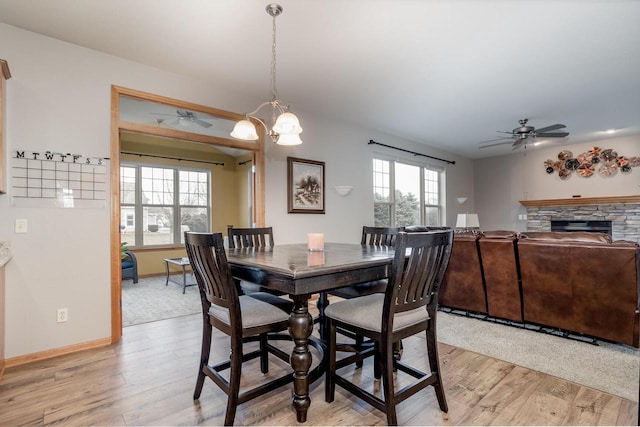 dining space featuring ceiling fan, a stone fireplace, and light wood-type flooring