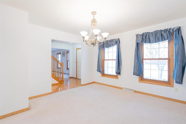 carpeted spare room with an inviting chandelier