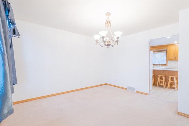 spare room featuring light colored carpet and a notable chandelier