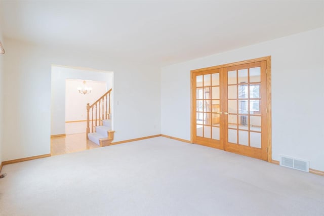 carpeted empty room with a chandelier and french doors