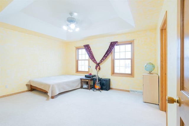 carpeted bedroom with ceiling fan and a tray ceiling