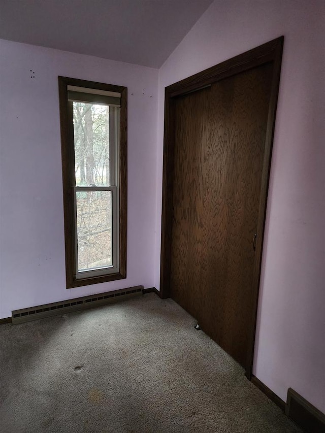 unfurnished bedroom featuring carpet, a baseboard heating unit, vaulted ceiling, and a closet